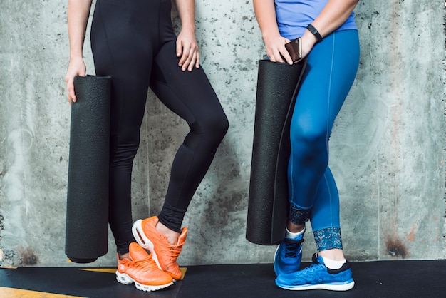 Vista de la sección baja de dos mujeres con colchoneta en el gimnasio