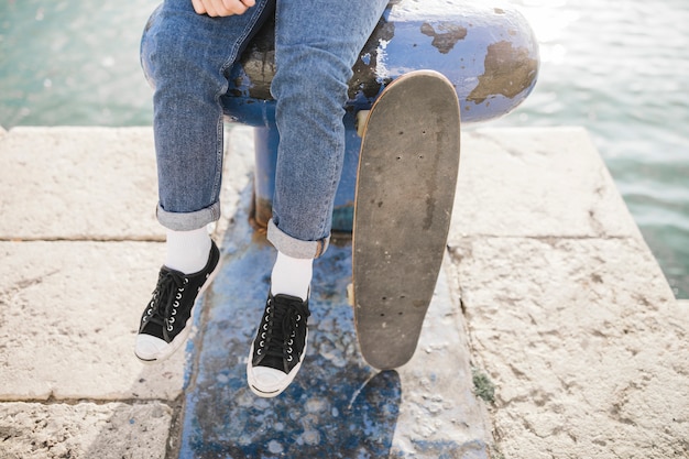 Foto gratuita vista de la sección baja de un hombre con patineta sentado en bolardo