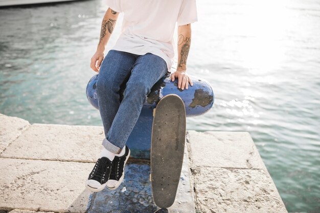 Vista de sección baja de un skater masculino sentado en bolardo con patín