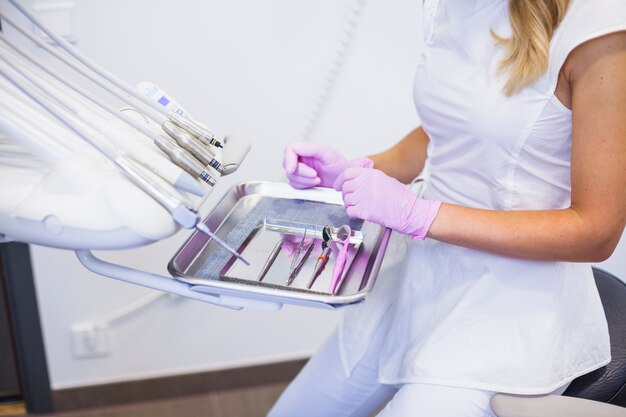 Vista de la sección media de la mano de un dentista que organiza herramientas dentales en la bandeja