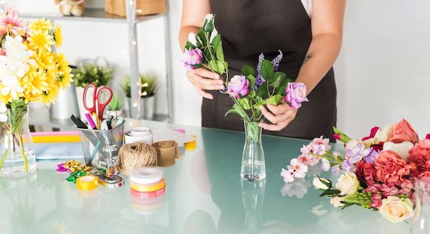 Vista de la sección media de una mano femenina clasificando flores en un jarrón en el escritorio