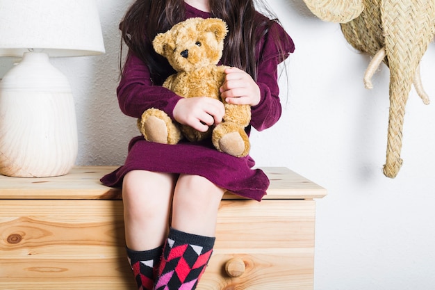 Vista de sección media de una niña sentada en la mesa con un muñeco de peluche