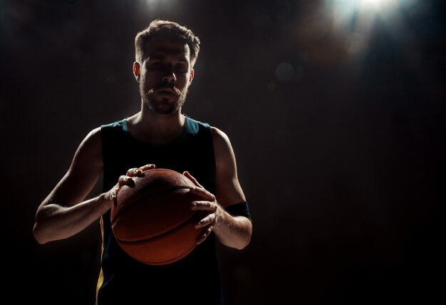 Vista de la silueta de un jugador de baloncesto con baloncesto en la pared negra