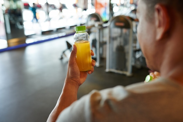 Foto gratuita vista sobre el hombro del hombre irreconocible sosteniendo una botella de jugo de naranja