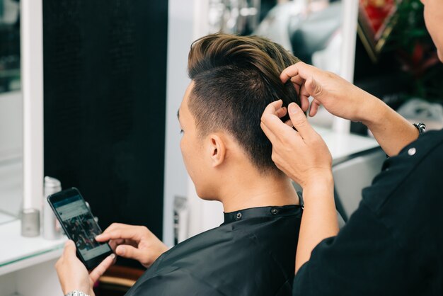 Vista sobre el hombro del peluquero recortado irreconocible que aplica cera en el cabello del cliente