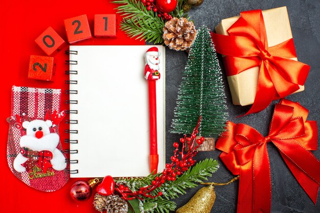 Vista superior de los accesorios de decoración de cuaderno espiral números de calcetín navideño de ramas de abeto en una servilleta roja y árbol de Navidad de regalo sobre fondo oscuro