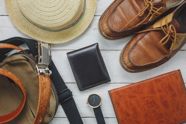 Vista superior de los accesorios para viajar con el concepto de ropa hombre. billetera en fondo de madera. reloj, bolso, sombrero, cuaderno y zapato en la mesa de madera blanca.