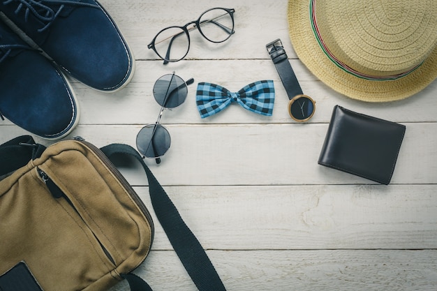 Vista superior de los accesorios para viajar con el concepto de ropa hombre. pajarita, billetera en fondo de madera. reloj, gafas de sol, bolsa, sombrero y zapatos en la mesa de madera.