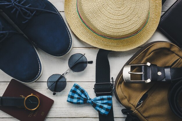 Vista superior de los accesorios para viajar con el concepto de ropa hombre. pajarita, billetera en fondo de madera. reloj, gafas de sol, bolsa, sombrero y zapatos en la mesa de madera.