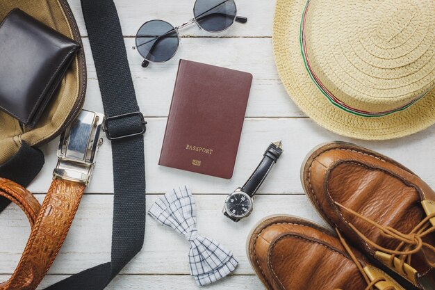 Vista superior de los accesorios para viajar con el concepto de ropa hombre. pajarita, billetera en fondo de madera. reloj, gafas de sol, bolsa, sombrero y zapatos en la mesa de madera.