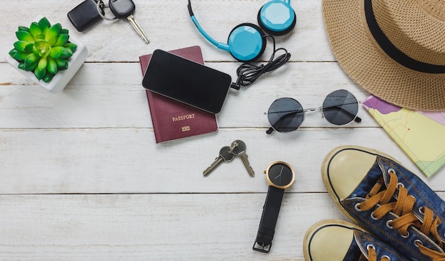 Vista superior de los accesorios para viajar concepto. teléfono móvil escuchando música por auriculares sobre fondo de madera.shoes, pasaporte, reloj, gafas de sol y sombrero sobre la mesa de madera.