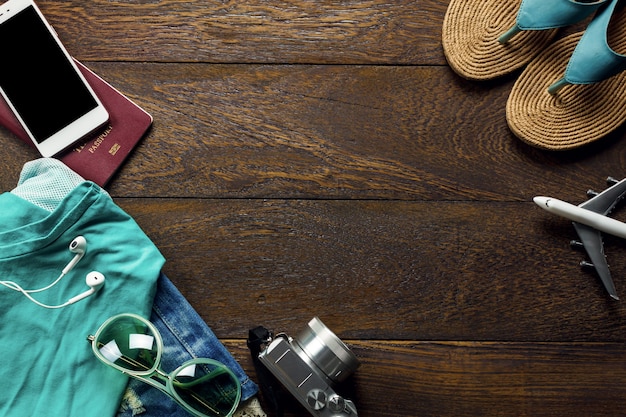 Vista superior de accesorios de viaje con teléfono móvil, cámara, gafas de sol, mujer de tela, sandalia sobre tabla de madera con espacio de copia. Concepto de viaje.