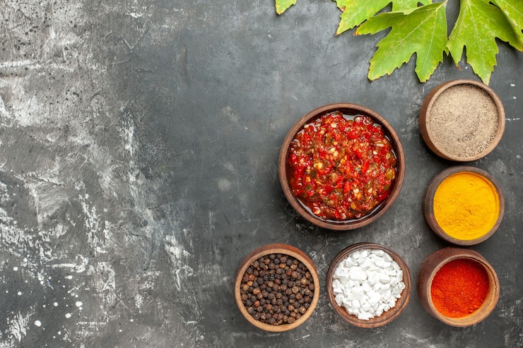 Foto gratuito vista superior adjika delicioso en cuenco de madera diferentes especias en cuencos pequeños sobre fondo gris