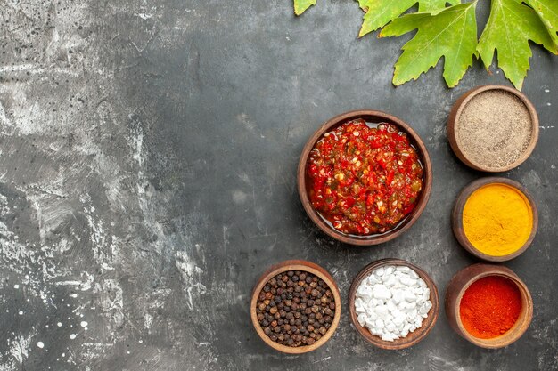 Vista superior adjika delicioso en cuenco de madera diferentes especias en cuencos pequeños sobre fondo gris