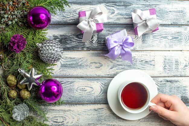 Vista superior adornos de Navidad una taza de té en mano femenina pequeños regalos ramas de abeto juguetes de Navidad sobre fondo de madera