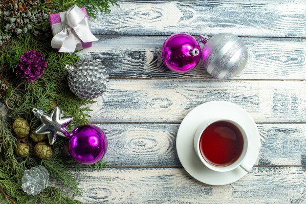 Vista superior adornos navideños regalo pequeño ramas de abeto juguetes navideños una taza de té en la superficie de madera