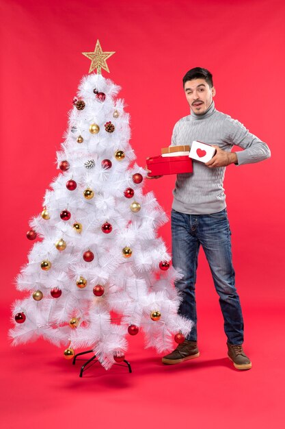 Vista superior del adulto joven en una blusa gris de pie cerca del árbol de Navidad blanco decorado