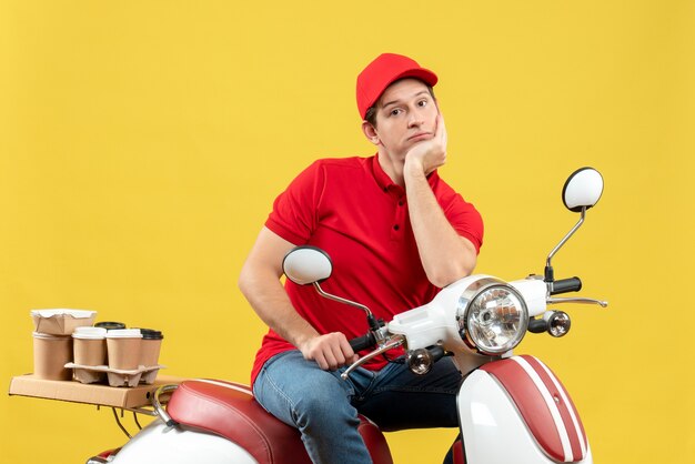 Vista superior del adulto joven con blusa roja y sombrero entregando orden en pensamientos profundos sobre fondo amarillo