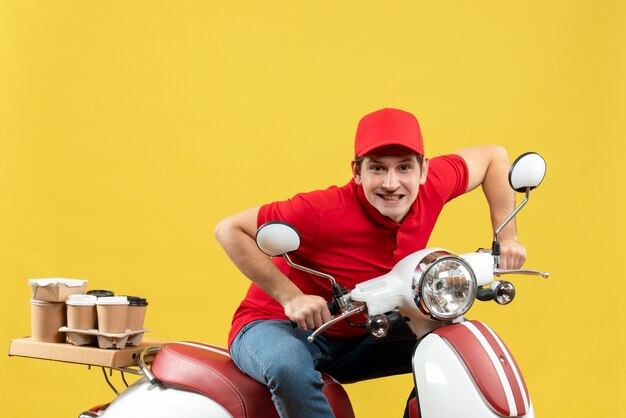 Vista superior del adulto joven concentrado vistiendo una blusa roja y un sombrero entregando pedidos sobre fondo amarillo