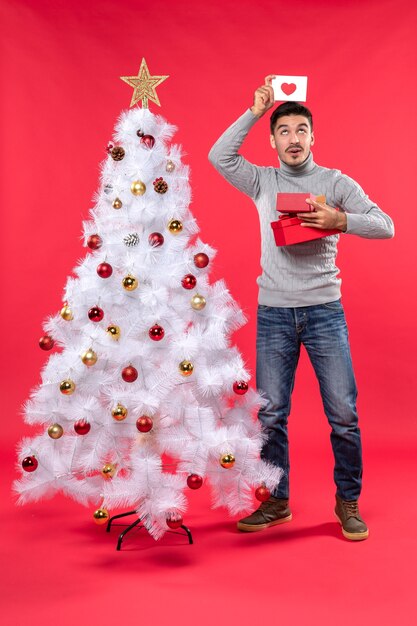 Vista superior del adulto romántico en una blusa gris de pie cerca del árbol de Navidad blanco decorado
