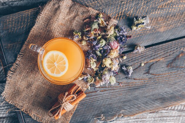 Vista superior de agua de color naranja en la taza con limón y té en tela de saco y fondo de madera oscura. horizontal