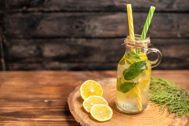 Vista superior de agua de desintoxicación fresca en un vaso servido con tubos y limones en el lado izquierdo en una bandeja marrón