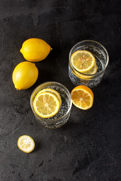 Una vista superior de agua con limón bebida fresca fresca con limones en rodajas dentro de vasos transparentes en el fondo oscuro cóctel bebida fruta