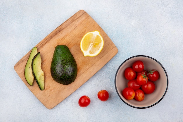 Vista superior de aguacate fresco en tablero de cocina de madera con tomates lemonnd en un tazón en blanco