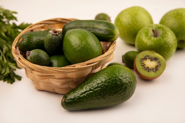 Vista superior de aguacates con pepino en un balde con manzanas verdes y kiwi aislado sobre una superficie blanca