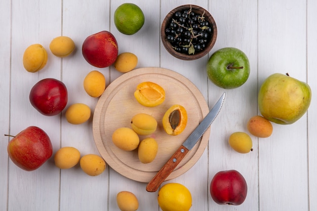 Foto gratuita vista superior de los albaricoques en un soporte con un cuchillo melocotones manzanas y grosellas negras en un recipiente sobre una superficie blanca