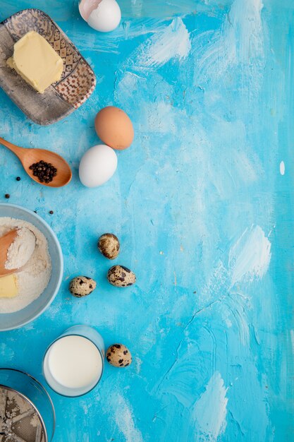 Vista superior de alimentos como harina de mantequilla de huevo con leche y pimienta negra sobre fondo azul con espacio de copia