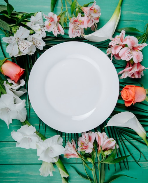 Foto gratuita vista superior de alstroemeria de color blanco y coral y rosas con gladiolos y alcatraces dispuestos alrededor de un plato blanco sobre fondo de madera verde