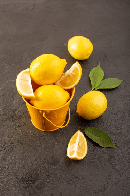 Una vista superior amarillo limones frescos suaves y jugosos enteros y en rodajas dentro de la cesta amarilla con hojas verdes sobre el fondo oscuro frutas color cítrico
