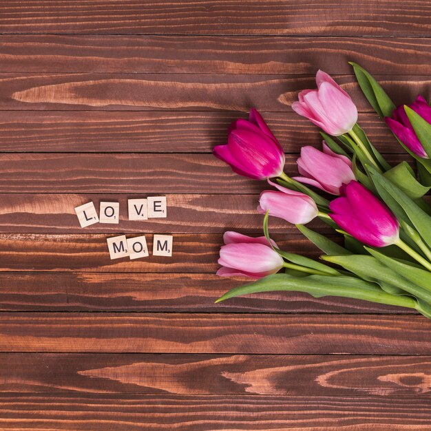 Vista superior del amor; mamá; Texto con flores de tulipán rosa en el escritorio de madera