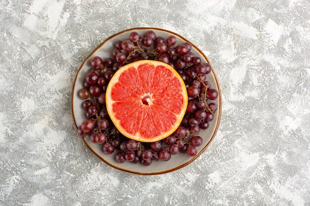 Vista superior anillo de pomelo fresco con uvas rojas en el escritorio blanco