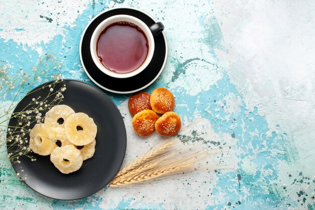 Vista superior de los anillos de piña seca con una taza de té y pequeños pasteles en el fondo azul fruta piña azúcar dulce seco