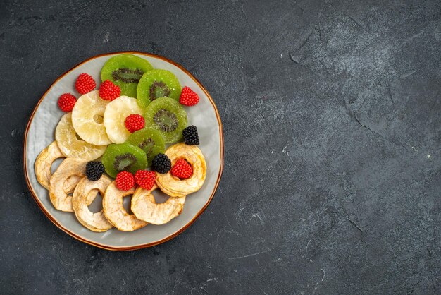 Vista superior de anillos de piña secos con kiwis secos y manzanas sobre la superficie gris oscuro