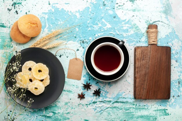 Vista superior de los anillos de piña secos con una taza de té en el escritorio azul pastel hornear galletas de frutas galletas de azúcar dulce