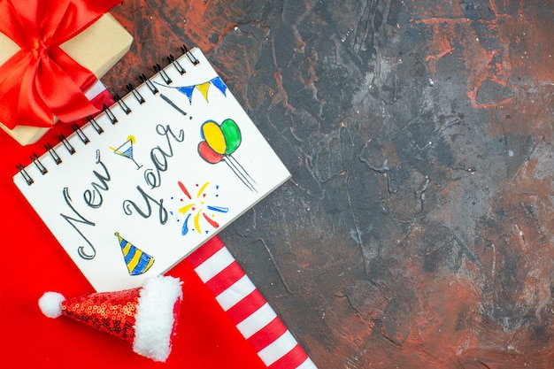 Vista superior año nuevo escrito en Bloc de notas mini gorro de Papá Noel sobre mantel rojo en el espacio libre de la mesa rojo oscuro