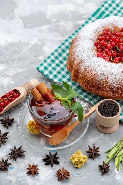 Una vista superior de arándanos rojos frescos agrios y suaves con té de pastel redondo y canela en el escritorio blanco bayas de frutas