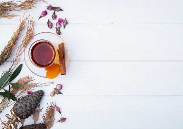 Vista superior de armudu vaso de té con albaricoques secos, canela y capullos de rosa secos esparcidos en blanco con espacio de copia