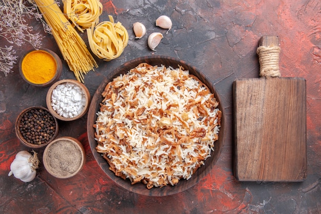 Vista superior del arroz cocido junto con los condimentos en la comida de la foto del plato de comida del escritorio oscuro