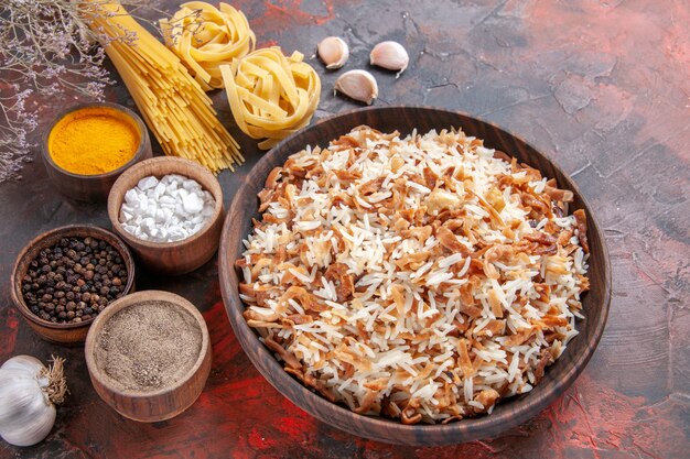 Vista superior del arroz cocido junto con los condimentos en la comida del plato de comida de superficie oscura