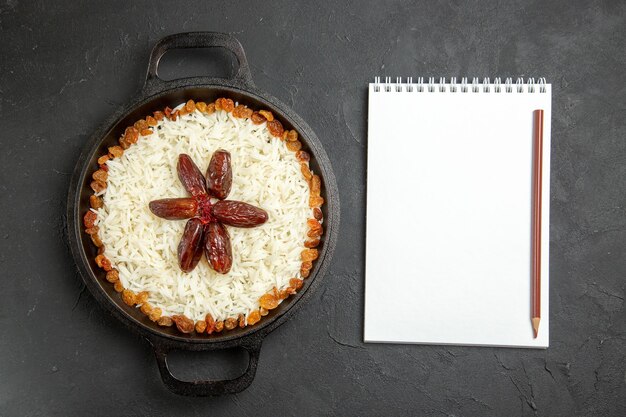 Vista superior de arroz cocido con pasas dentro de la sartén en la cena de comida oriental de arroz de superficie oscura