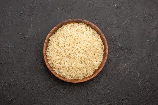 Vista superior del arroz crudo dentro de la placa marrón sobre la superficie gris