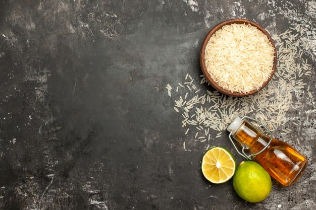 Vista superior de arroz crudo con limones y aceite en el piso oscuro color de la fruta de alimentos crudos