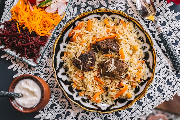Vista superior de arroz con zanahoria cocido con cordero servido con yogur y ensalada