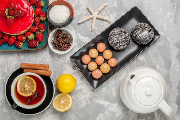 Vista superior de aspecto delicioso pastel pequeño pastel con taza de té galletas y fresas frescas en la superficie de color blanco claro pastel galletas galletas crema dulce