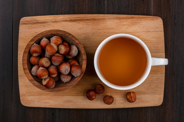 Vista superior de la avellana en un recipiente con una taza de té en una pizarra sobre una superficie de madera