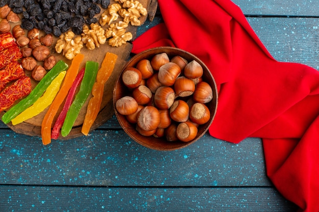 Vista superior de avellanas enteras frescas con nueces y jaleas en el escritorio azul